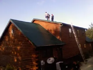 Crew on the ridge of a green metal roof on a two story log home in Bethany Beach