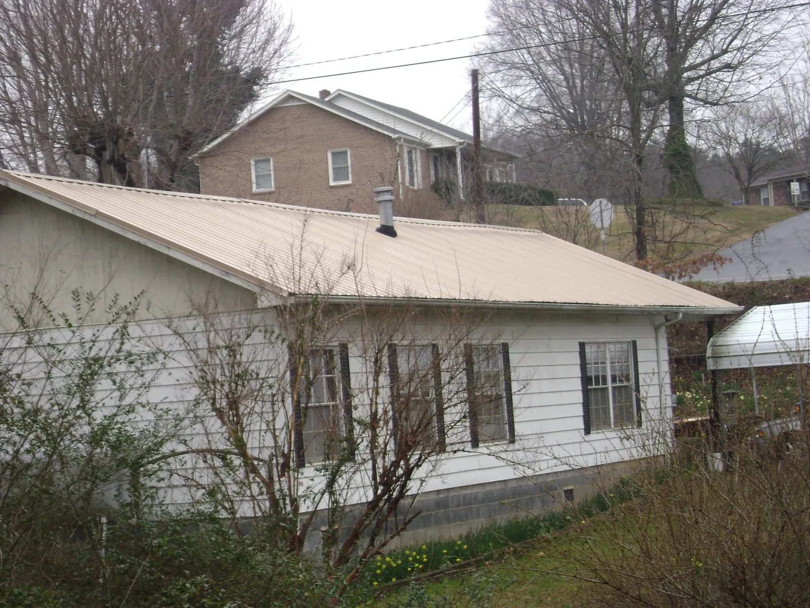 Tan metal roof on a white sided house set into a hillside — Commercial Roofing by Roofing Brothers in Bethany Beach